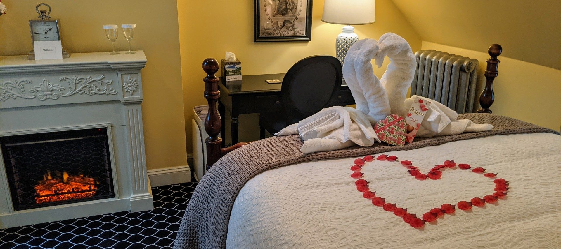 bed covered with folded towels and rose petals, electric fire place is lit