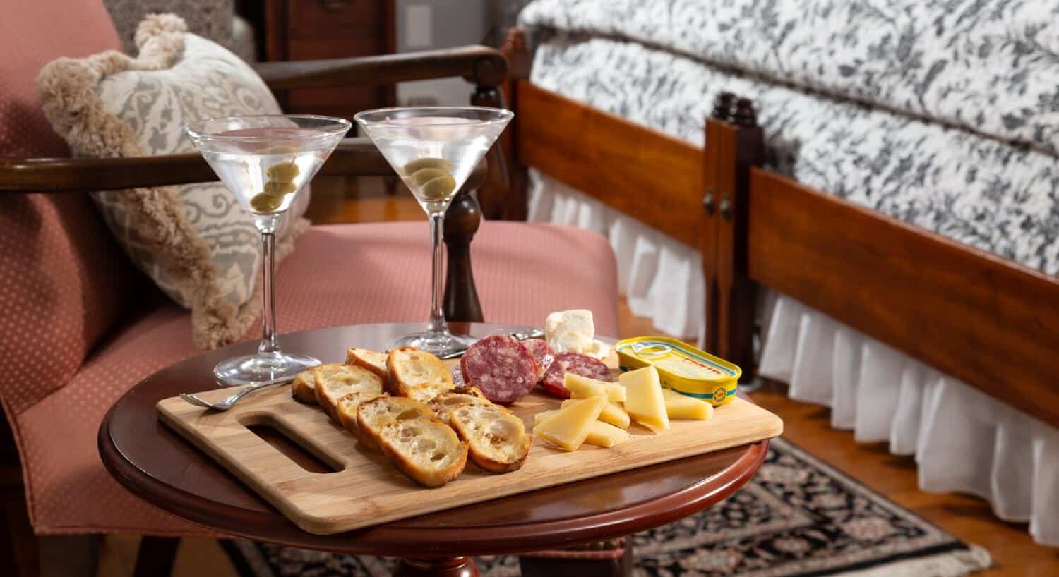 A wooden side table holding platter of cheese, meats and bread with two martinis