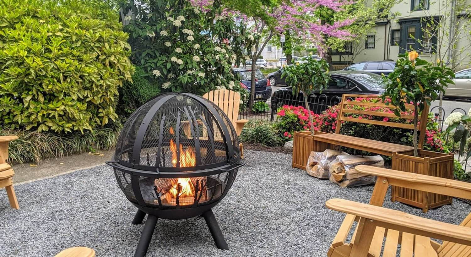 Metal globe outdoor fire pit on a stone patio surrounded by wooden adirondack chairs