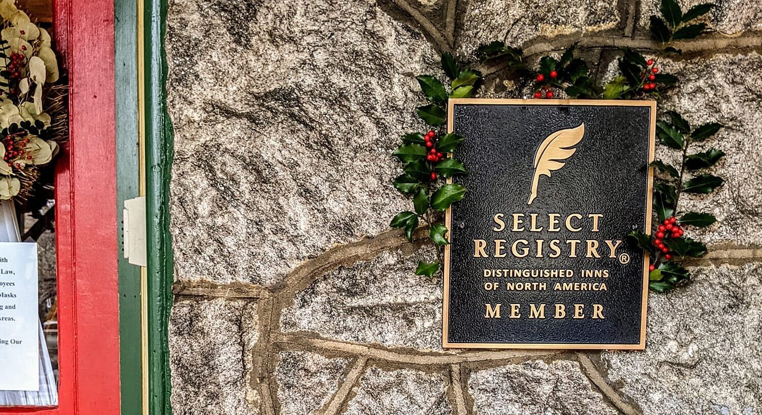 Black sign with gold text and logo hanging on a stone wall outside a green and red door