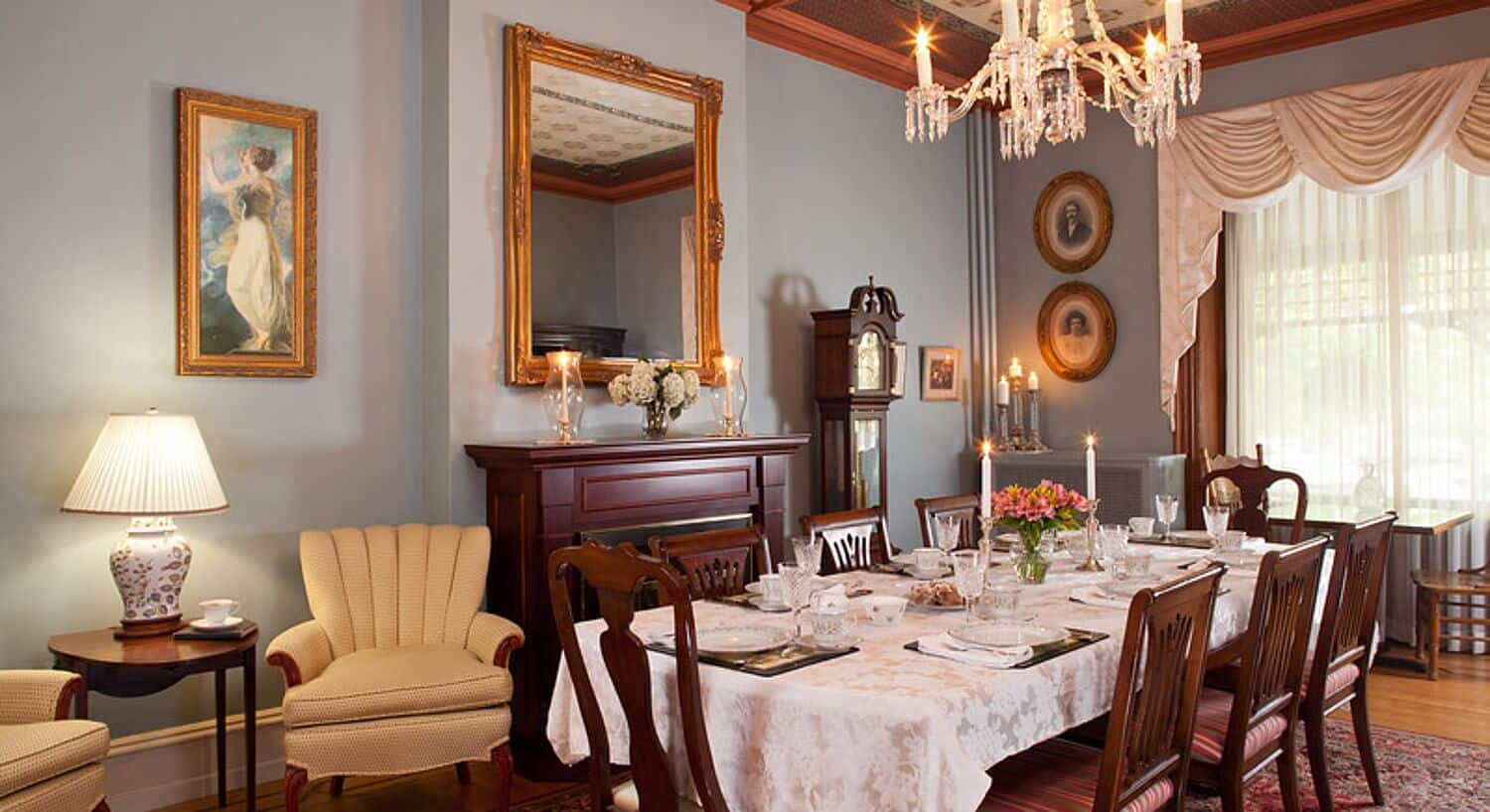 Large dining room with table set for eight, chandelier above and sitting chairs next to brown fireplace