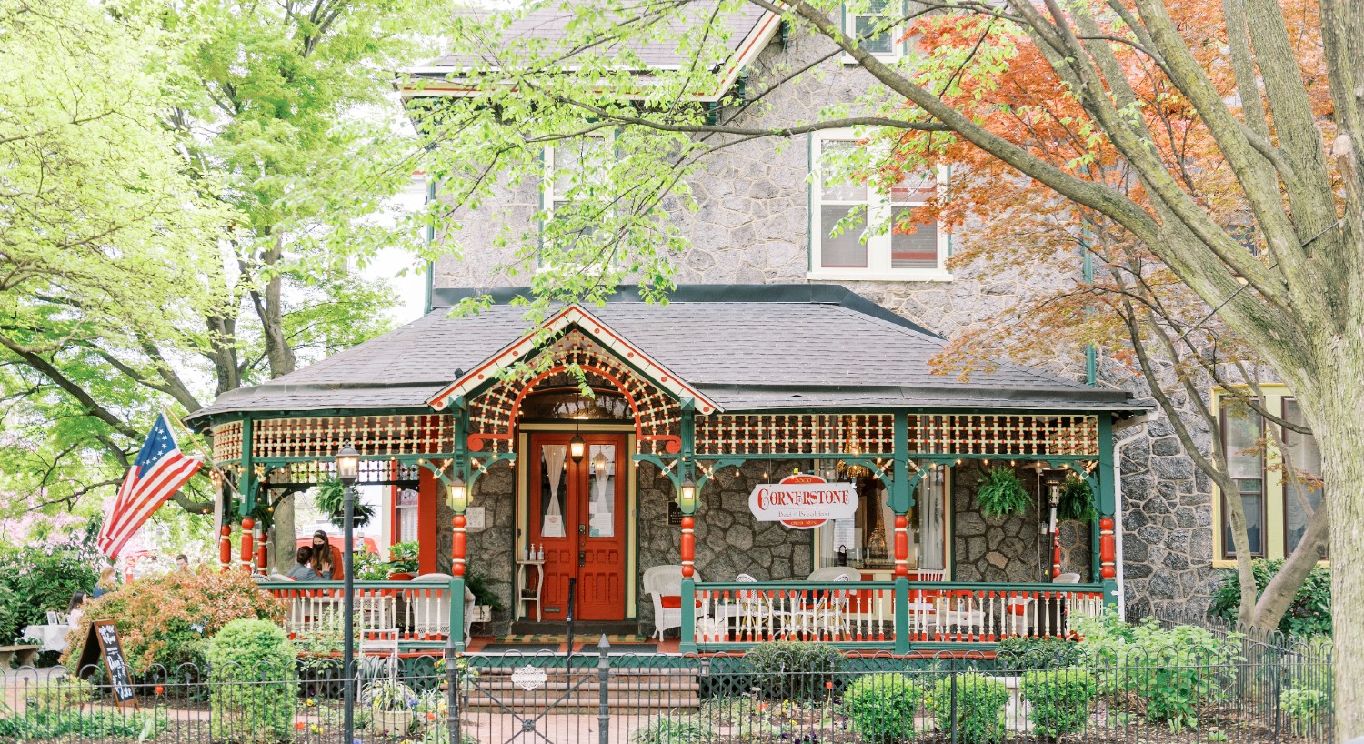 Front facade of a beautiful historic, stone home with wrap around porch and red front door