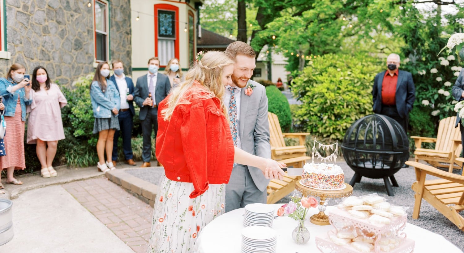 A couple cutting a wedding cake on an outdoor patio with people looking on