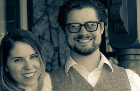 A man in glasses, shirt and vest standing next to a woman with long brown hair