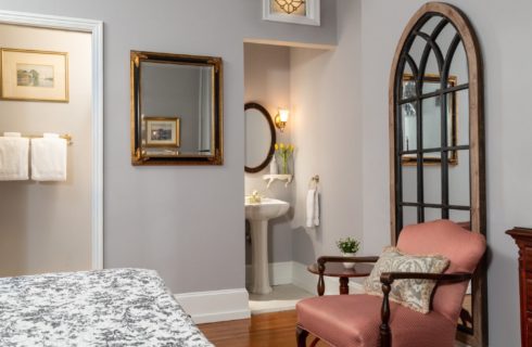 Guest room with bed, sitting chair and pedestal sink with mirror in corner cove