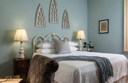 Guest room with white bed, side tables with lamps, desk and chair and blue walls