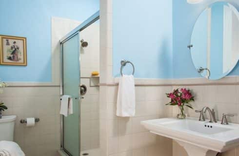 Bathroom with toilet, stand up shower and white pedestal sink under a large round mirror