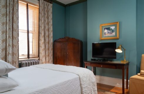 Bedroom with queen bed, brown armoire and desk with TV and lamp