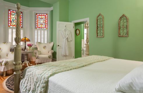 Large bedroom with four poster bed, sitting area with chairs by large, colorful stained glass windows