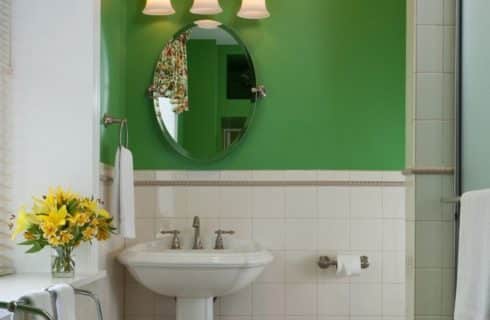 One white pedestal sink under an oval mirror in bathroom with white tile and green walls