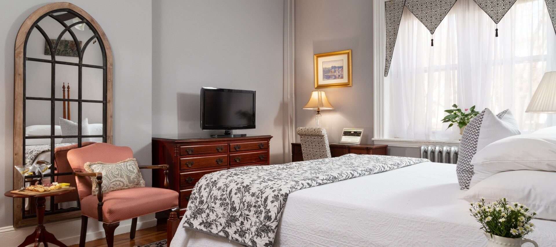 Guest room with white bed, large windows, dresser with TV and pink sitting chair