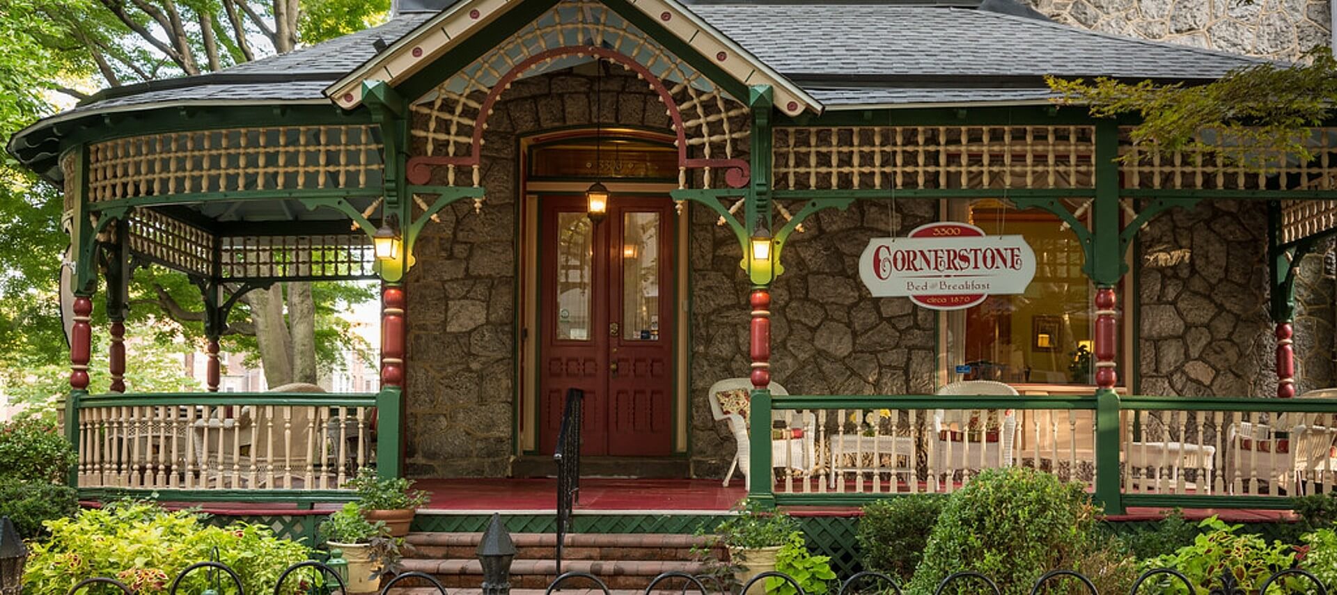 Front facade of a home with stone walls and large wrap around porch painted green and red