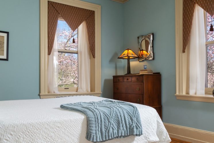 Guest room with white bed, two large windows, dresser and sitting desk with chair