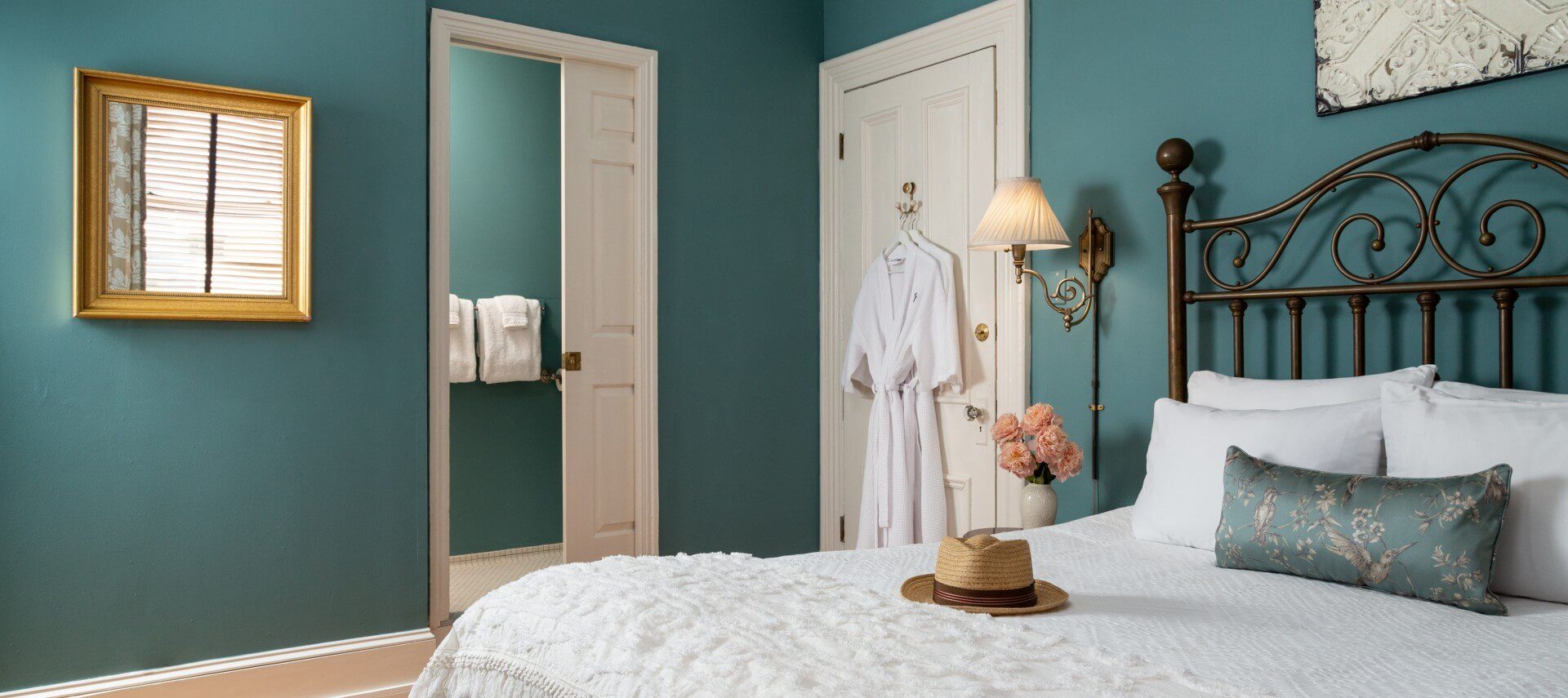 Bedroom featuring queen bed with wrought iron headboard, wall lamps and doorway into private bath