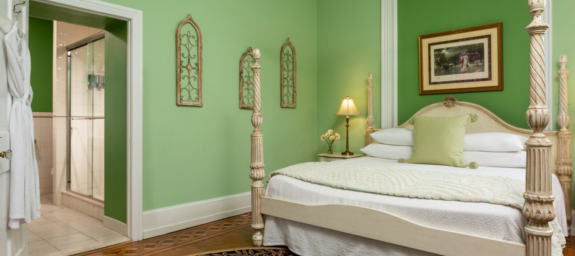 Large bedroom with four poster bed, green walls and doorway into bathroom with hanging robes