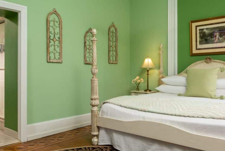 Large bedroom with four poster bed, green walls and doorway into bathroom with hanging robes