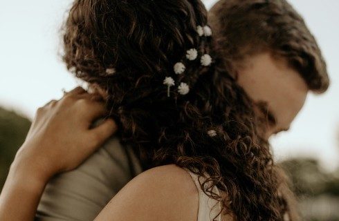 A woman with tiny white flowers in her hair hugging a man in a brown shirt