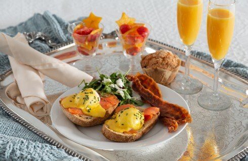 Silver platter holding a plate of breakfast, a muffin and two flutes of orange juice