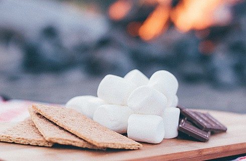 A wooden platter holding graham crackers, marshmallows and pieces of chocolate