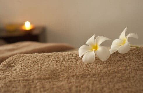 A brown towel with two white and yellow flowers an a candle lit in the background