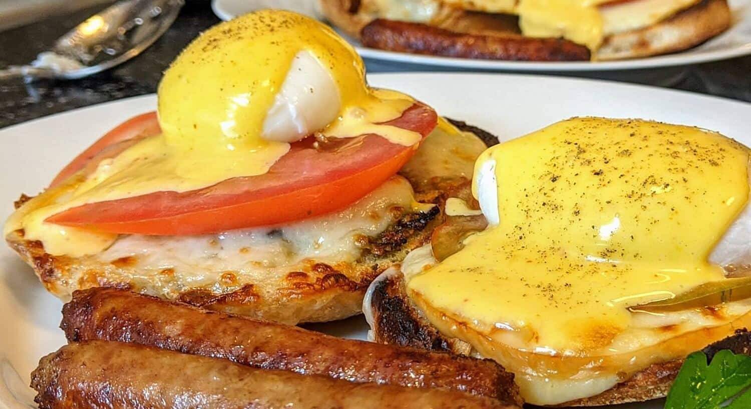 White plate of breakfast with sausage, muffins and eggs with hollandaise sauce