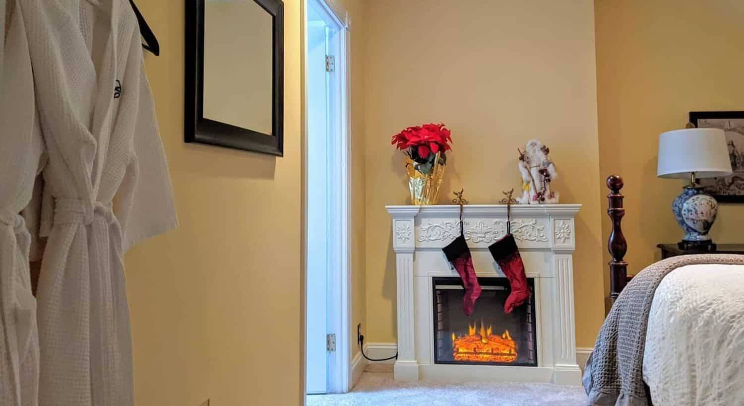 Small white electric fireplace with two hanging stockings in a guest room with yellow walls