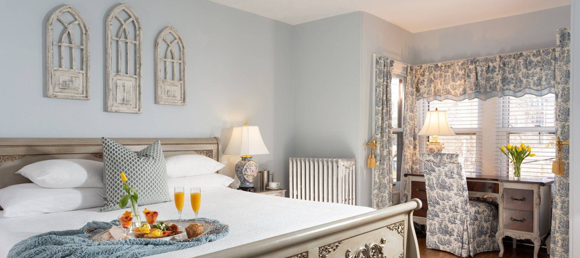 Guest room featuring king bed with a breakfast tray and writing desk with chair in nook with windows