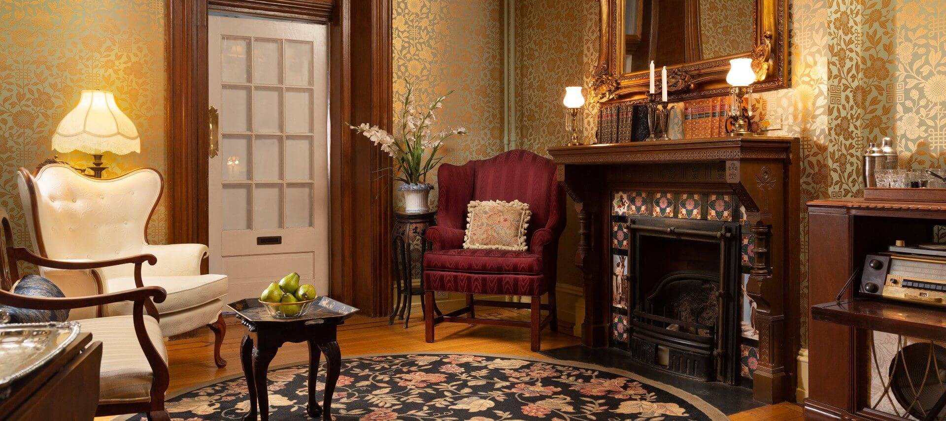Living room of a home with an array of antique furniture, fireplace and gold decorative wallpaper